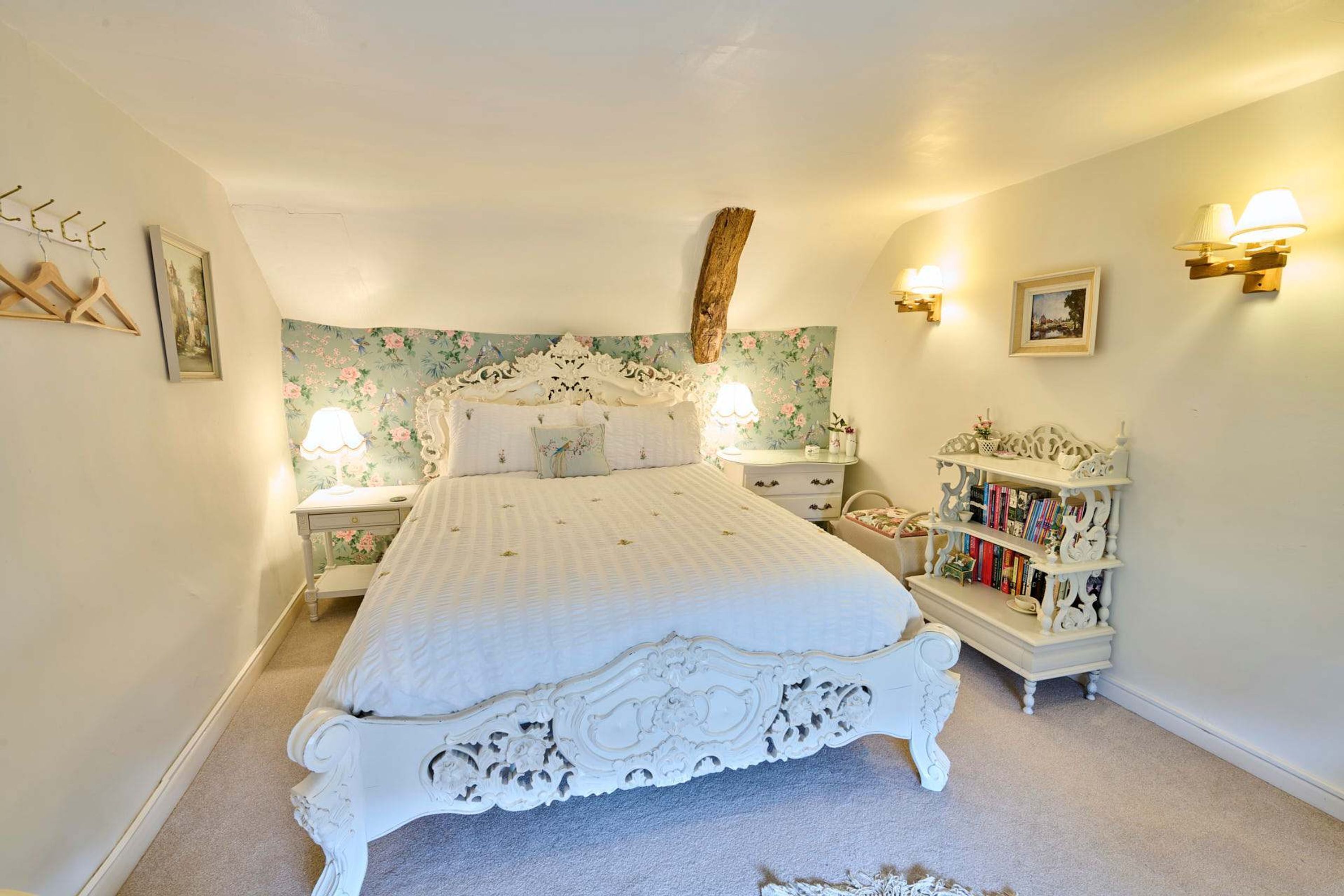 Une chambre à coucher avec un grand lit, deux tables de chevet, une commode, une bibliothèque et des appliques murales décoratives.