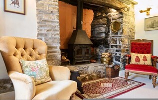 Una chimenea de piedra tradicional con estufa de leña, un sillón tapizado rojo y un sillón con cojines.