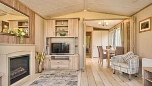 A cozy living room with a fireplace, a TV, and a dining area with a table and chairs. - Host Stay Fern Lodge (Ipswich)