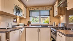 A compact kitchen with white cabinets, a built-in microwave, a stove, and a window with blinds. - Host Stay Fern Lodge (Ipswich)