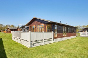 Eine Holzhütte mit umzäuntem Garten, großen Fenstern und strahlend blauem Himmel.