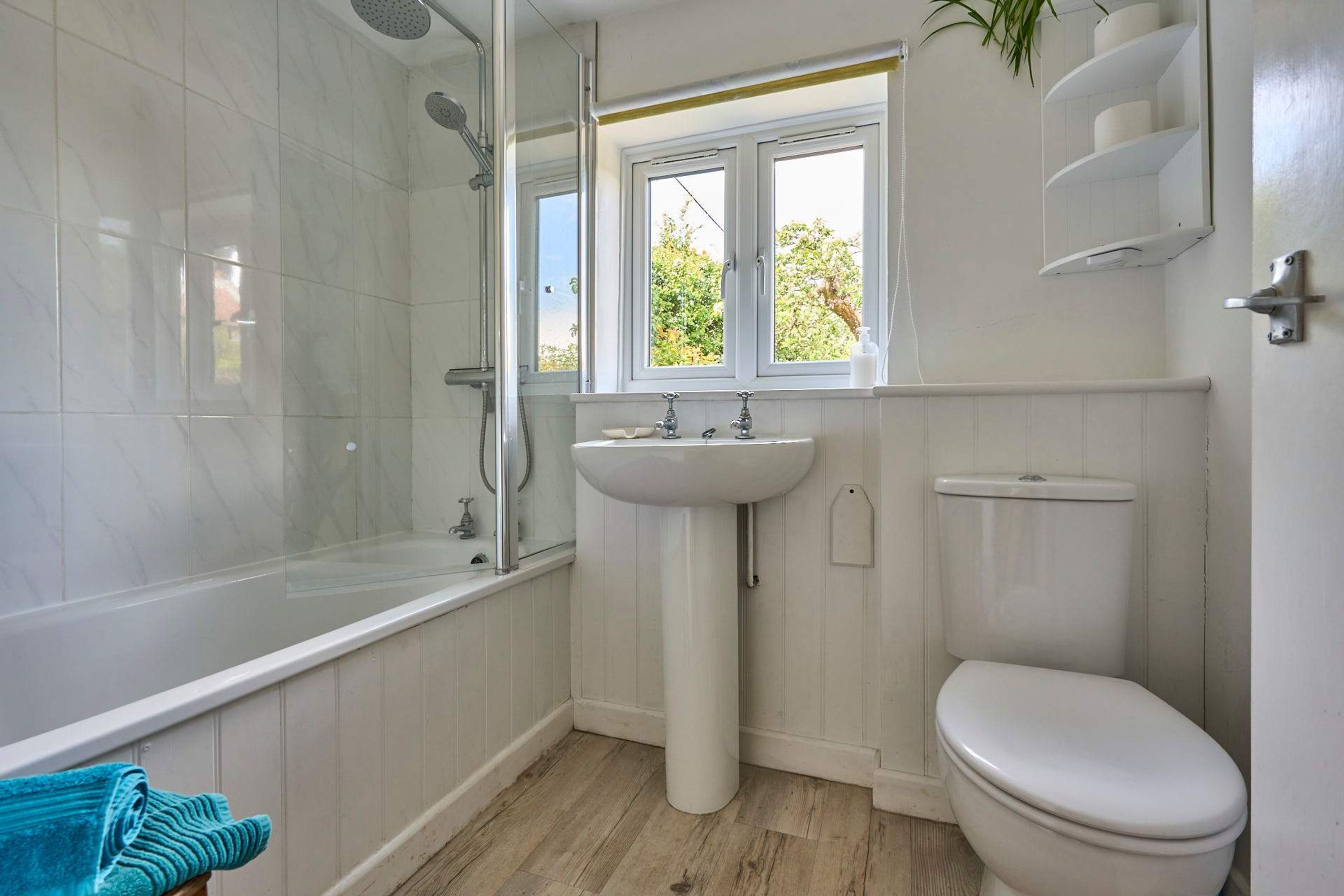 A bathroom with a bathtub, sink, toilet, and a window with a view of greenery.