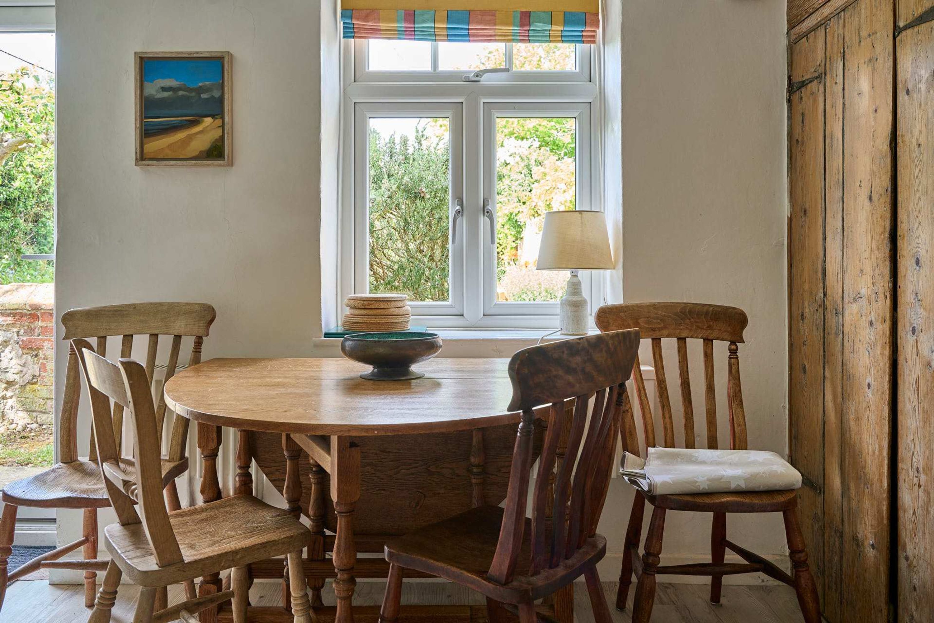 Uma sala de jantar com uma mesa de madeira redonda, quatro cadeiras de madeira, uma tigela e um abajur.