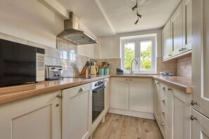 A kitchen with a microwave, toaster, oven, and a window with a view of greenery. - Host Stay Teal Cottage (King's Lynn)