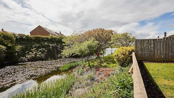 A garden with a pond, wooden fence, and a house in the background.