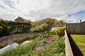 A garden with a pond, wooden fence, and a house in the background. - Host Stay Stille House (Chathill)