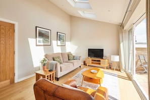 A modern living room with a sofa, coffee table, TV, and artwork on the wall. - Host Stay Stille House (Chathill)