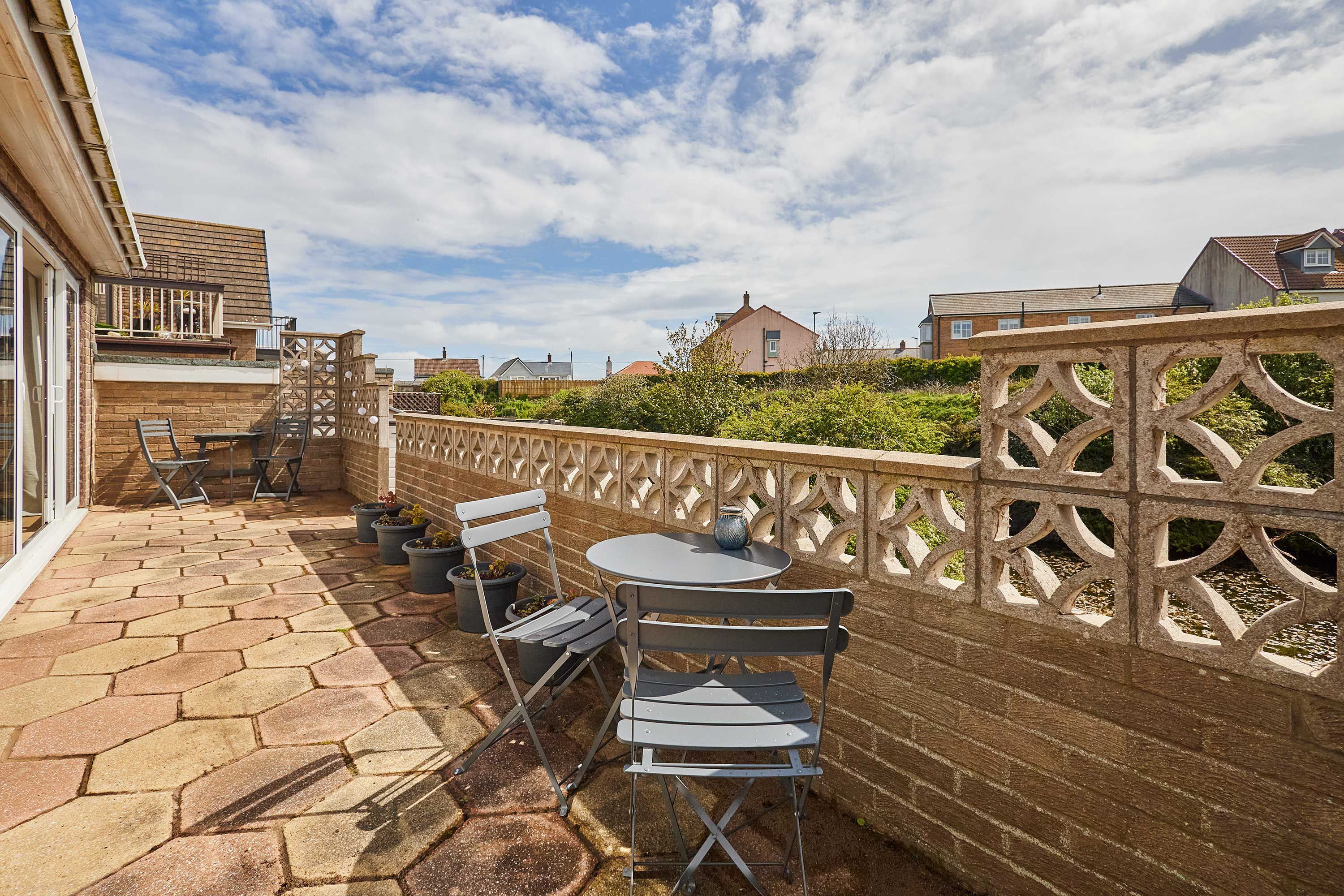 Un patio con una mesa y sillas, un muro de ladrillo y una valla decorativa.