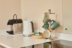 A kitchen counter with a coffee maker, a kettle, a mug rack, and a bowl of snacks. - Host Stay Stille House (Chathill)