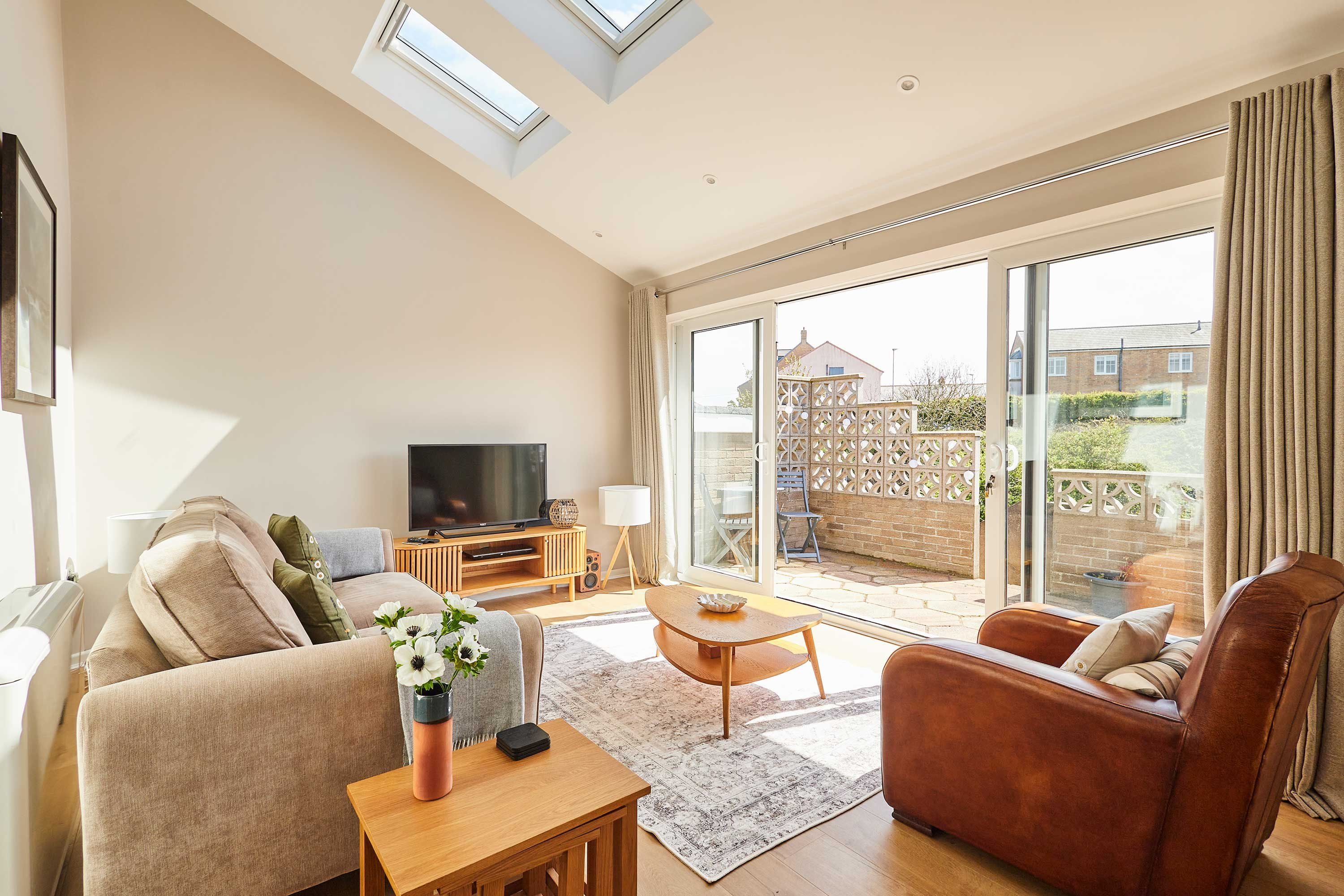 A spacious living room with a sofa, armchair, and coffee table, a TV, and a large sliding glass door leading to an outdoor area.