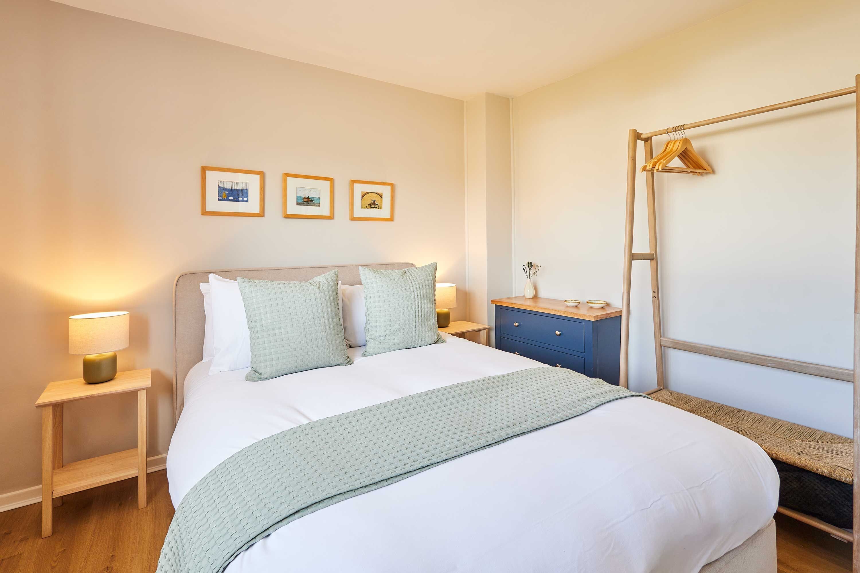Ein ordentlich eingerichtetes Schlafzimmer mit Bett, Nachttischen, einem Kleiderschrank und einer Kleiderstange.