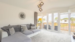 Ein modernes Wohnzimmer mit Ecksofa, Deckenleuchte und Blick durch große Schiebetüren auf eine Terrassenfläche.