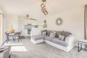 Ein modernes Wohnzimmer mit einer Eckcouch, einem Esstisch mit Stühlen, einer Küchenzeile und einem großen Spiegel an der Wand.