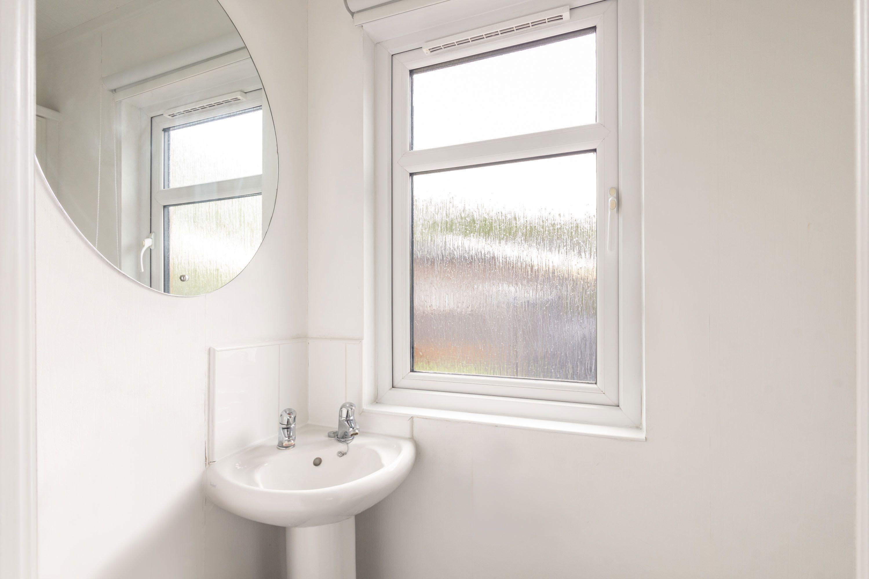 A bathroom with a white sink, a mirror, and a window with a view of a grassy field.