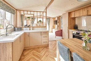 A modern kitchen with wooden cabinets, a built-in stove, and a dining area with a table and chairs. - Host Stay Molly s Place (Morpeth)