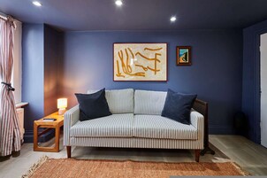 Una habitación con un sofá a rayas, una mesita con una lámpara y una obra de arte en la pared.