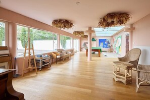 Ein geräumiges Zimmer mit großen Fenstern, Holzboden und Korbmöbeln.