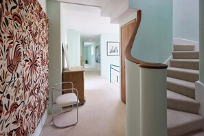 A staircase with a wooden handrail, a white chair, and a patterned wall. - Host Stay Joldwynds (Dorking)