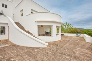 A modern white building with a curved exterior, a staircase leading to an upper level, and a patio area with a view of the landscape. - Host Stay Joldwynds (Dorking)