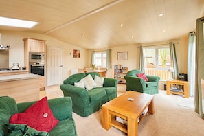 A spacious living area with green sofas, a wooden coffee table, and a kitchen in the background. - Host Stay Pine View (Windermere)