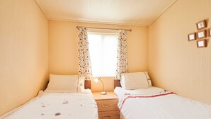 Ein Schlafzimmer mit zwei Betten, einem Nachttisch, einem Fenster mit Vorhängen und gerahmten Bildern an der Wand.