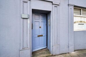 Eine blaue Tür mit einem Messingklopfer, darüber ein Schild für 'Little Globe Apartments' und ein Fenster mit der Aufschrift 'Alex Sherwood Solicitors'.