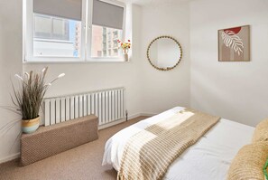 Ein Schlafzimmer mit Bett, Fenster mit Blick, Heizkörper, Wandspiegel und einem gerahmten Kunstwerk.