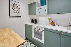 Eine Küche mit einem weißen Backofen, grünen Schränken, einem Holztisch und einem gerahmten Pflanzenmotiv an der Wand.