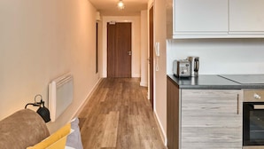 A hallway with a wooden floor, a kitchen area with a stove and toaster, and a door at the end.