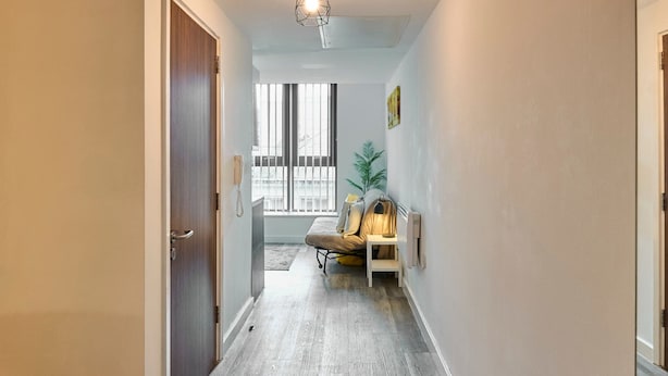 A hallway with a wooden floor, a bench, a potted plant, and a door on the left.