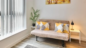 A living room with a sofa, a potted plant, a painting, and a lamp.