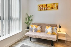 Ein Wohnzimmer mit einer Couch, einer Topfpflanze, einem Gemälde und einer Lampe.