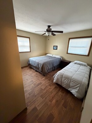 A bedroom with two beds, a ceiling fan, and a window with blinds.