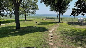 A grassy outdoor area with a paved path, trees, and a fenced area with a large cylindrical object. - Bluff’s Bend Retreat (Springfield)