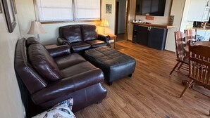 A living room with a sectional sofa, ottoman, and a dining area with wooden chairs. - Bluff’s Bend Retreat (Springfield)