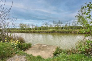 Ruhige Wasserfläche mit umgebender Bepflanzung und bewölktem Himmel.