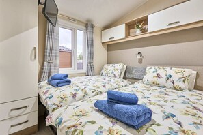 Ein Hotelzimmer mit zwei Betten, einem Fernseher, einem Fenster mit Vorhängen, einer Ablage mit Dekoration und einem Nachttisch.