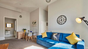 A living room with a blue sofa, a dining area with a table and chairs, and a kitchen in the background. - Host Stay Flat 2 Club Chambers (Malvern)