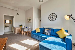 A living room with a blue sofa, a dining area with a table and chairs, a world map on the wall, and a clock. - Host Stay Flat 2 Club Chambers (Malvern)
