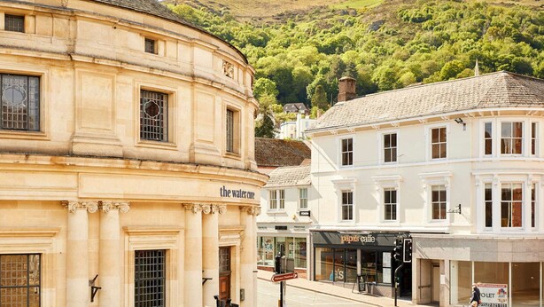A historic building with classical architecture, a street with shops, and a hillside in the background. - Host Stay Flat 2 Club Chambers (Malvern)