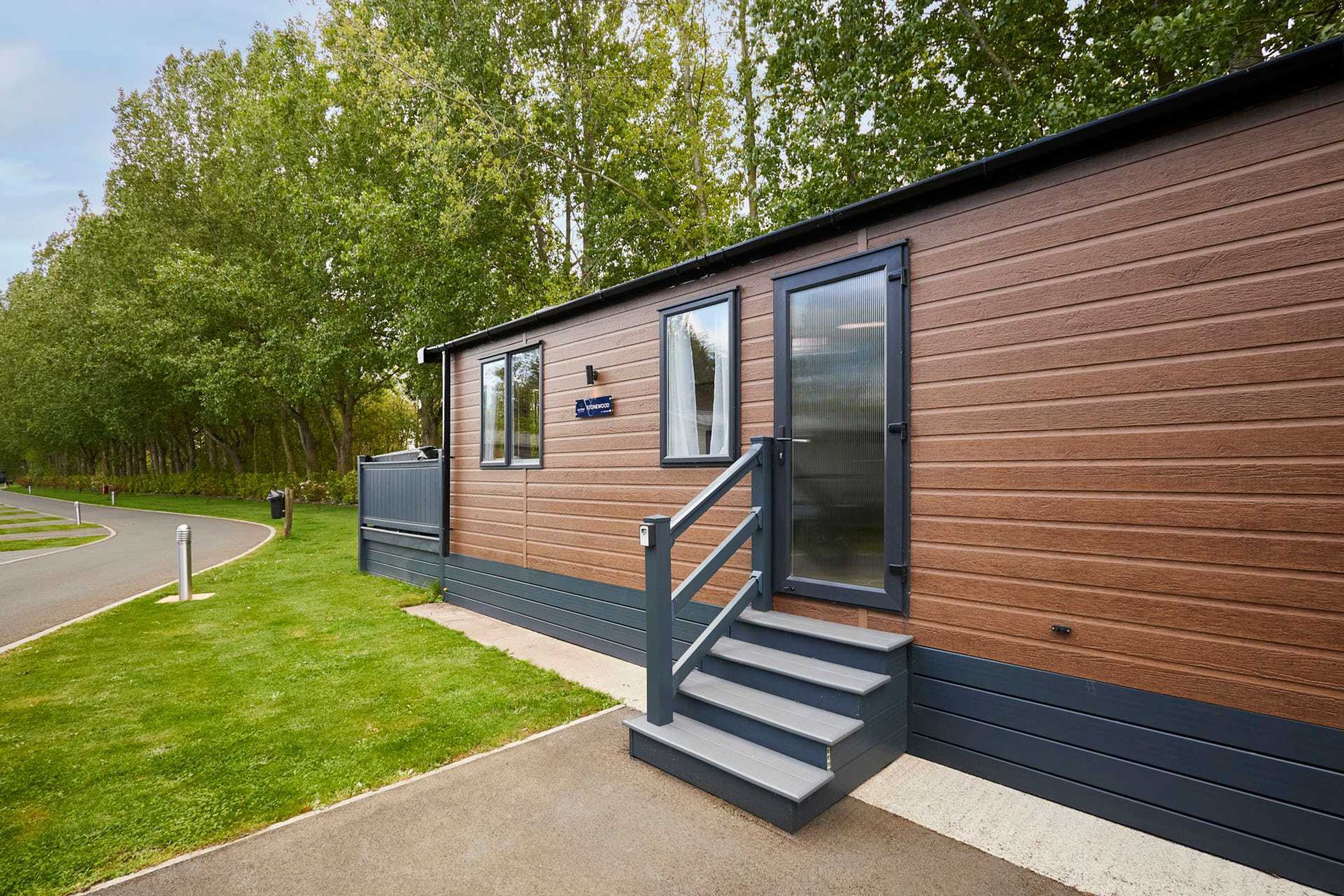 A single-story mobile home with a wooden exterior, a small porch, and a staircase leading to the entrance.