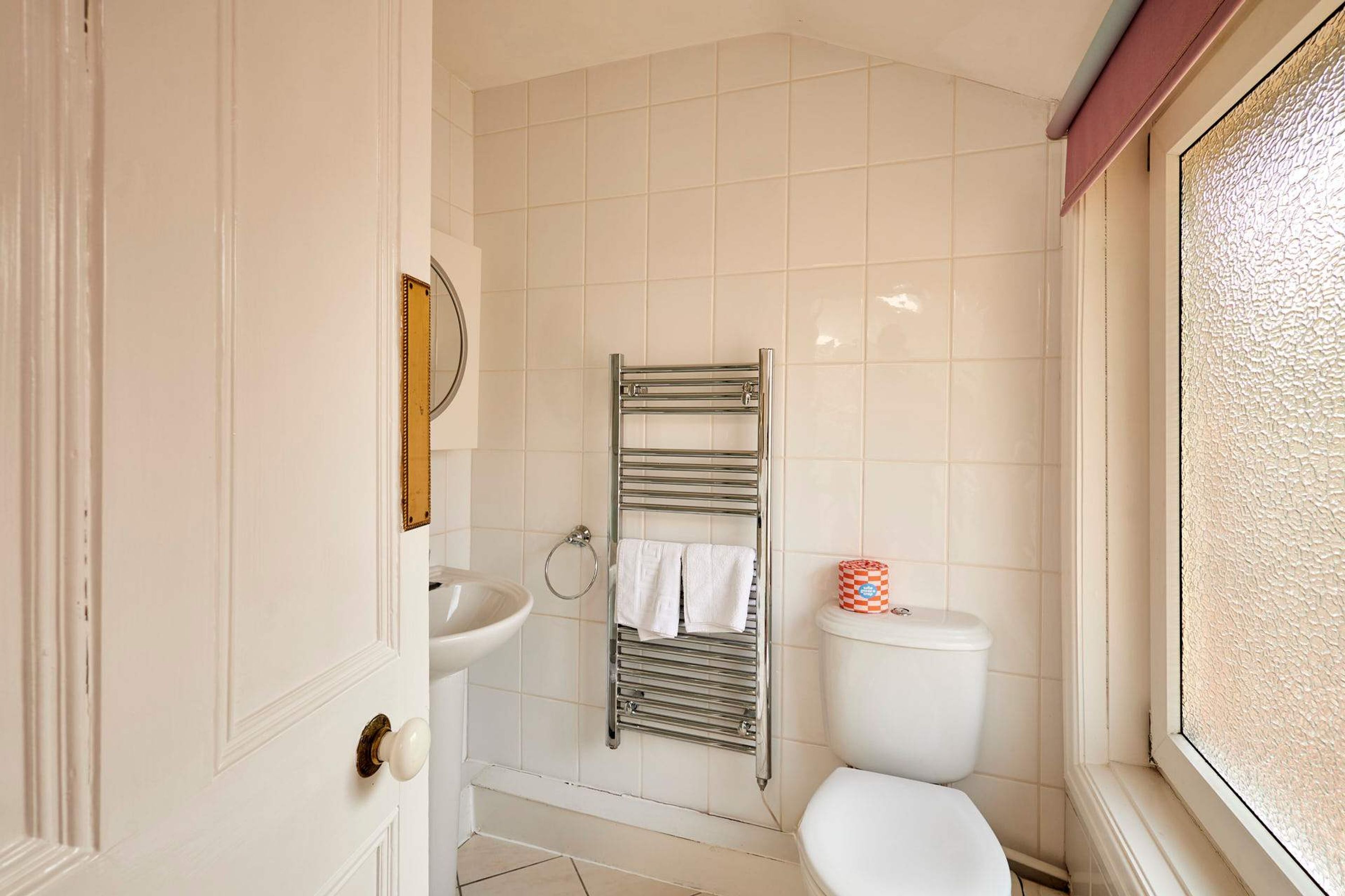 A bathroom with a white sink, a towel rack with two towels, a toilet, and a window with textured glass.