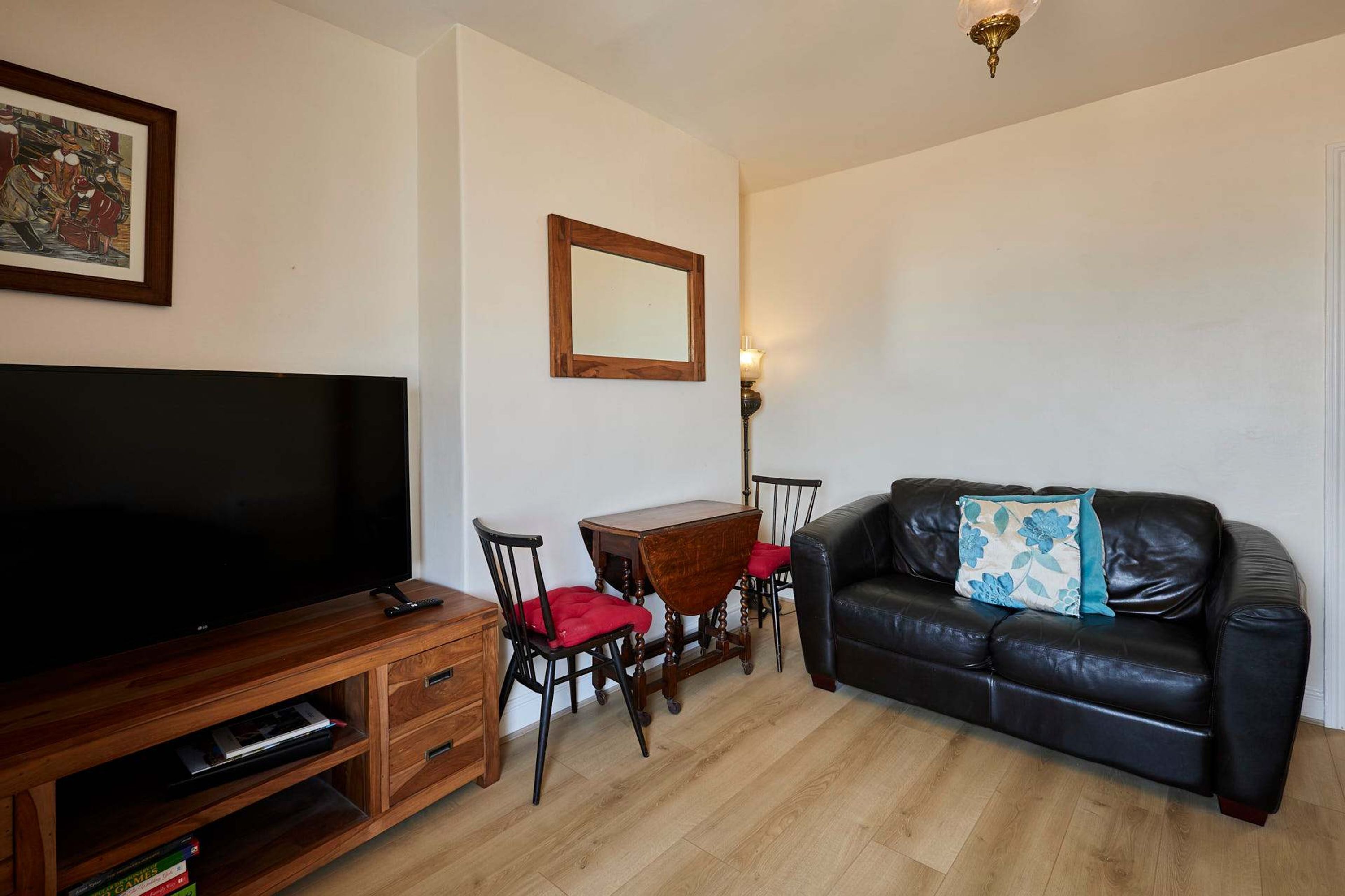 Un salon avec un téléviseur, des meubles en bois, un canapé en cuir noir et une table à manger avec des chaises.