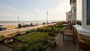 A coastal hotel with a view of the sea, a paved walkway, and a garden area.