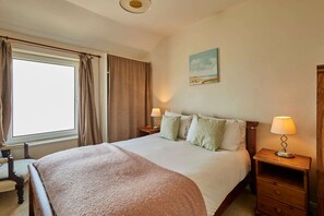 A neatly arranged bedroom with a large bed, two bedside tables with lamps, a chair, and a painting on the wall. - Host Stay The Beach (Filey)