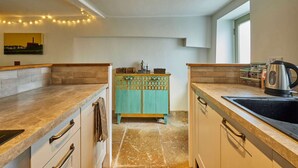 Una cocina con encimera de piedra, un mueble color turquesa y un hervidor sobre la encimera.