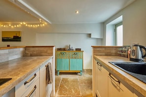 A kitchen with a stone floor, a teal cabinet, and a kettle on the counter. - Host Stay Lower Cross Lee Cottage (Todmorden)