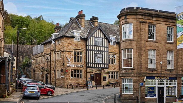 Un edificio tradicional con un pub llamado 'The White Hart' y una tienda llamada 'Hansons'.