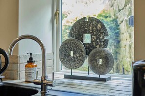 A bathroom with a sink, a hand soap dispenser, and two decorative stone pieces on a windowsill. - Host Stay Lower Cross Lee Cottage (Todmorden)