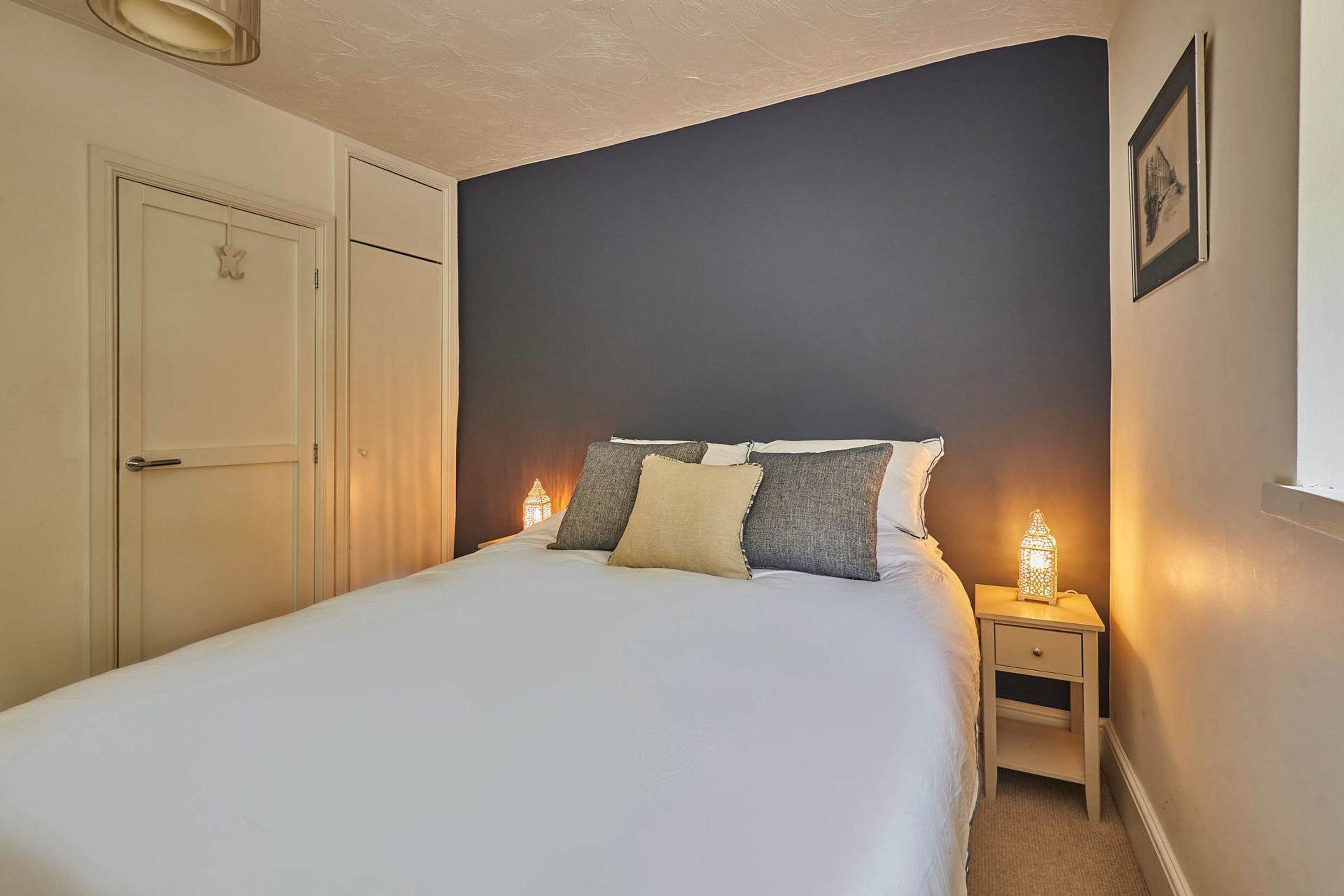 A bedroom with a bed, bedside lamps, a nightstand, a door, and a framed picture on the wall.